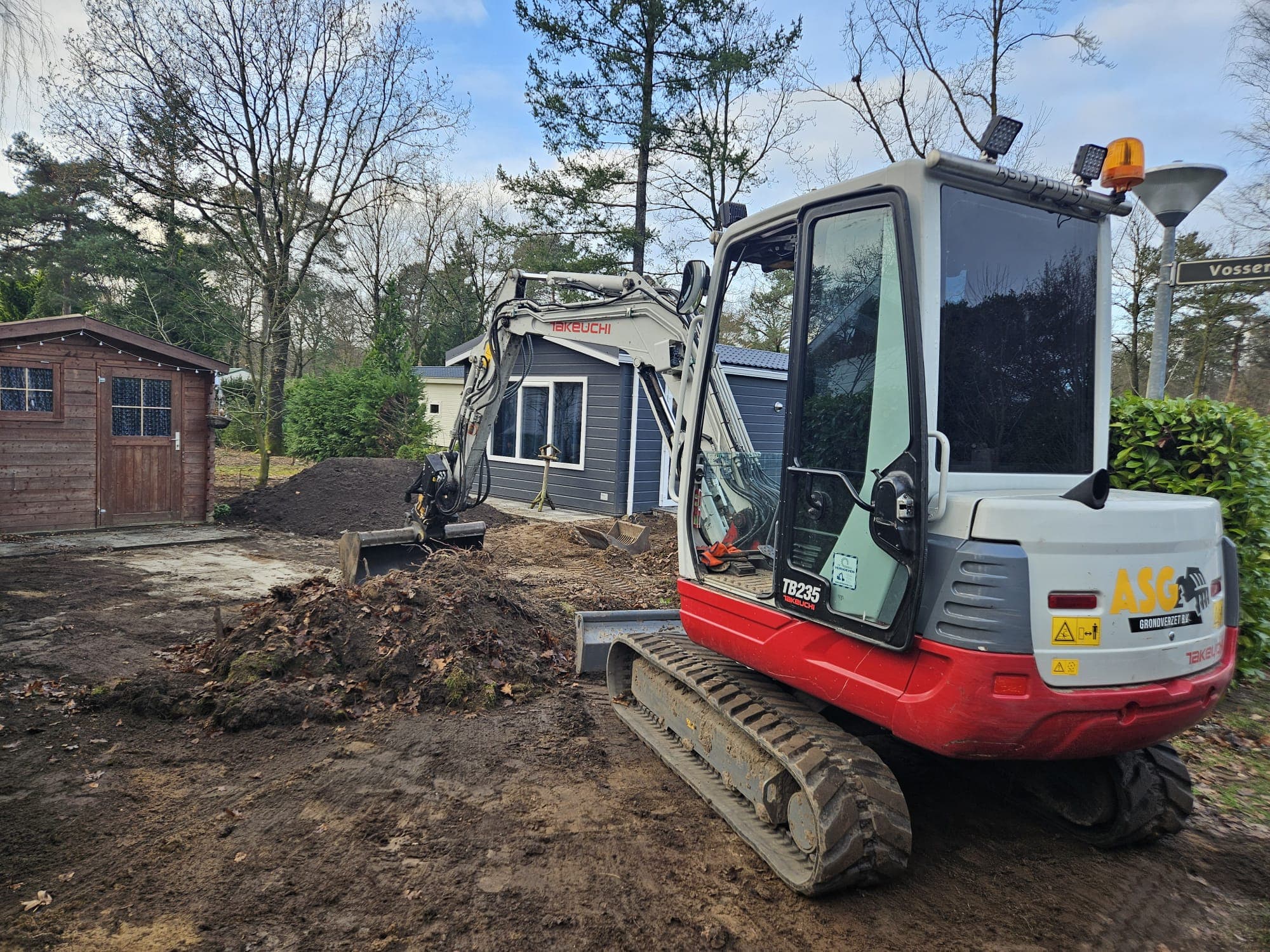 Minikraan tijdens tuin- en grondwerk naast chalet