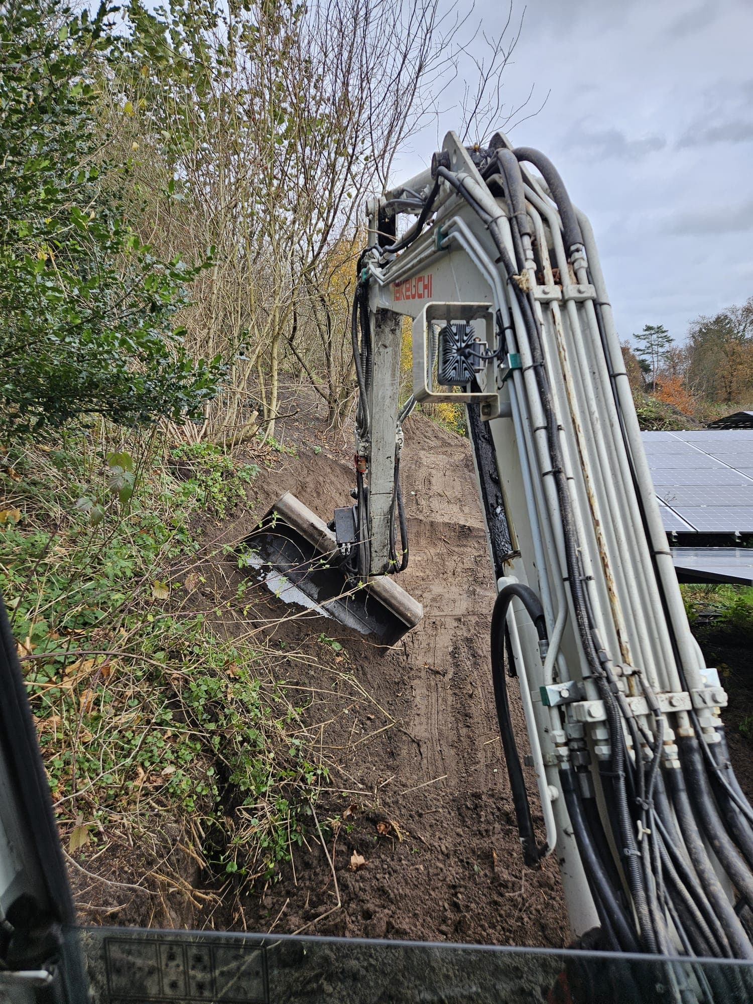 Minikraan werkt langs een talud en begroeiing