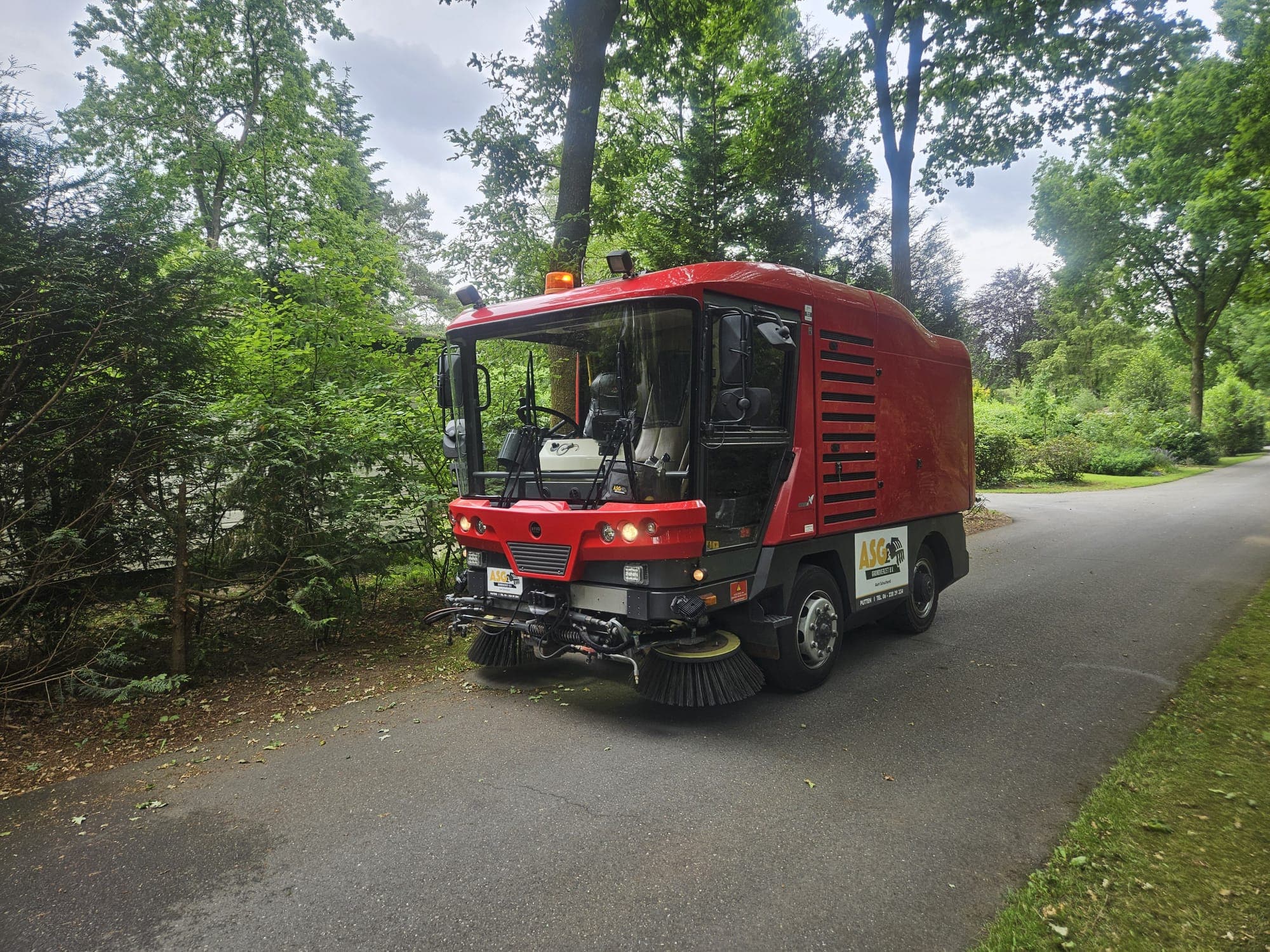 Rode veegmachine van ASG op een parkweg